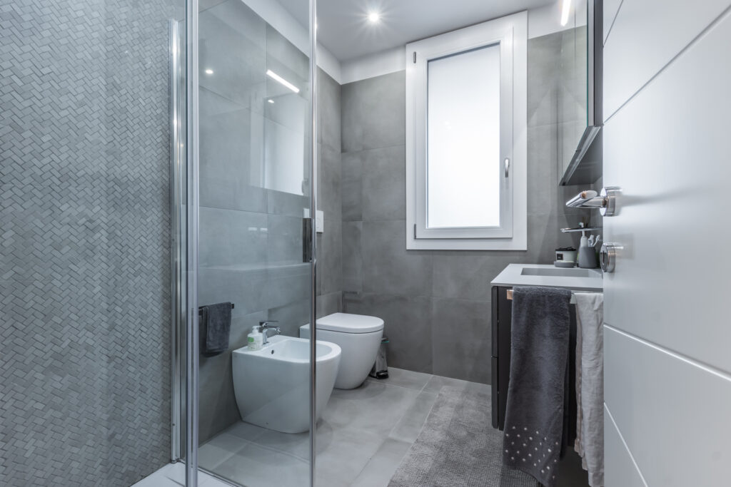 Bagno piccolo a Parma ristrutturato con soluzioni salvaspazio come sanitari sospesi e doccia walk-in, esempio di ingegneria dello spazio.