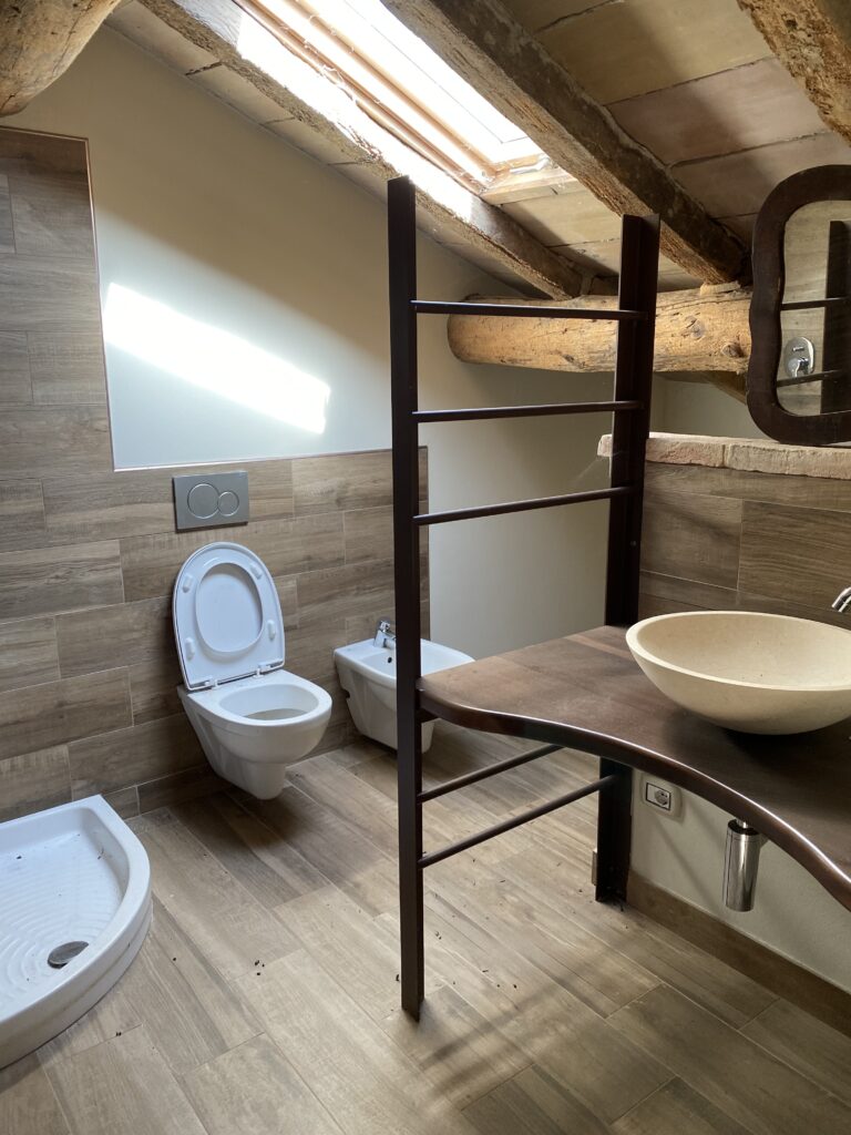 Mario Conte di CMG Crea Casa mostra come sfruttare un bagno mansardato a Parma con arredi su misura e travi a vista per ottimizzare lo spazio in un monolocale.