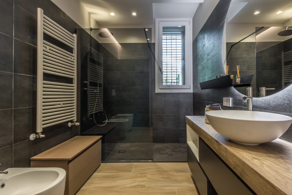 Mario Conte di CMG Crea Casa presenta una ristrutturazione bagno di lusso a Parma con rivestimenti scuri, doccia walk-in e grandi specchi per dare profondità all'ambiente.
